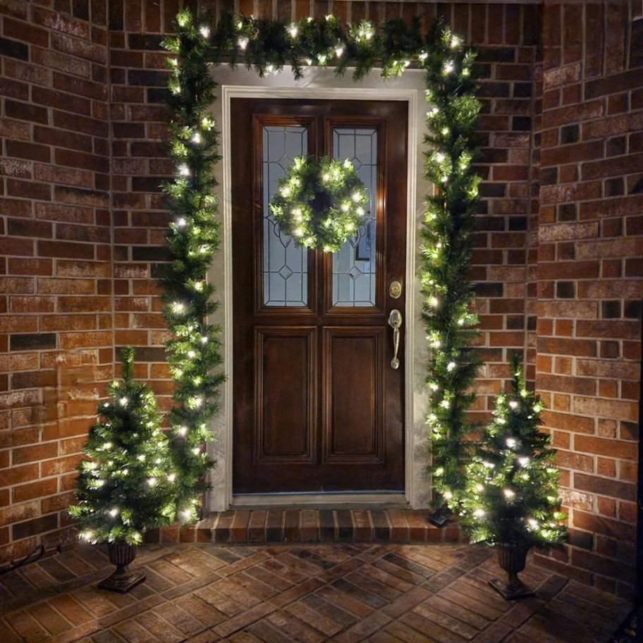 a front porch with matching Christmas decor set with garland, wreath and faux trees in pots