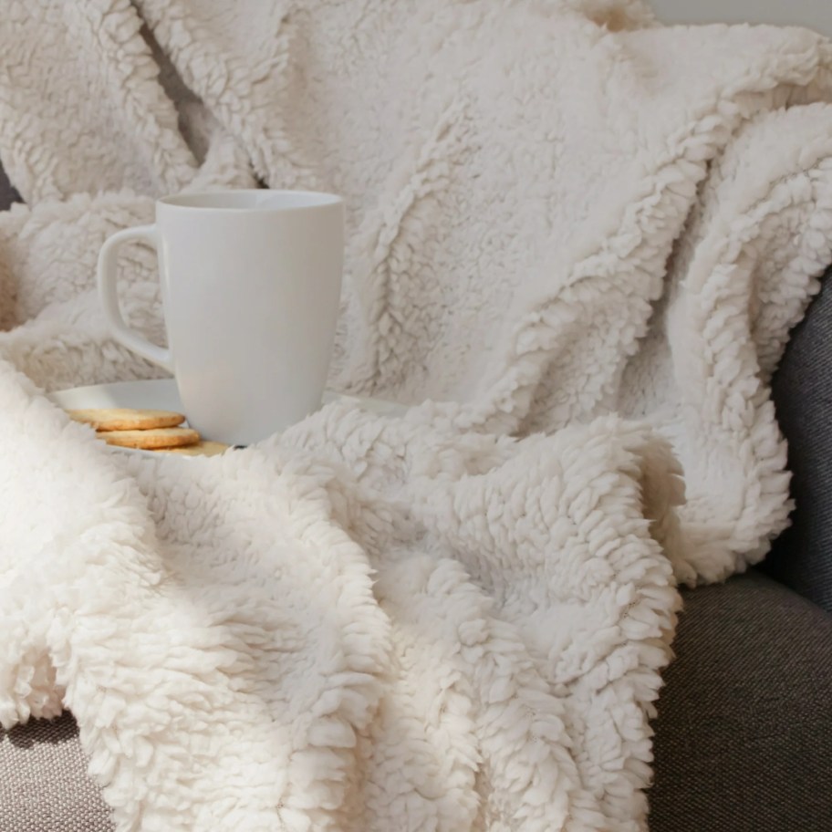 a white fuzzy style throw blanket on a chair with a white coffee mug on it