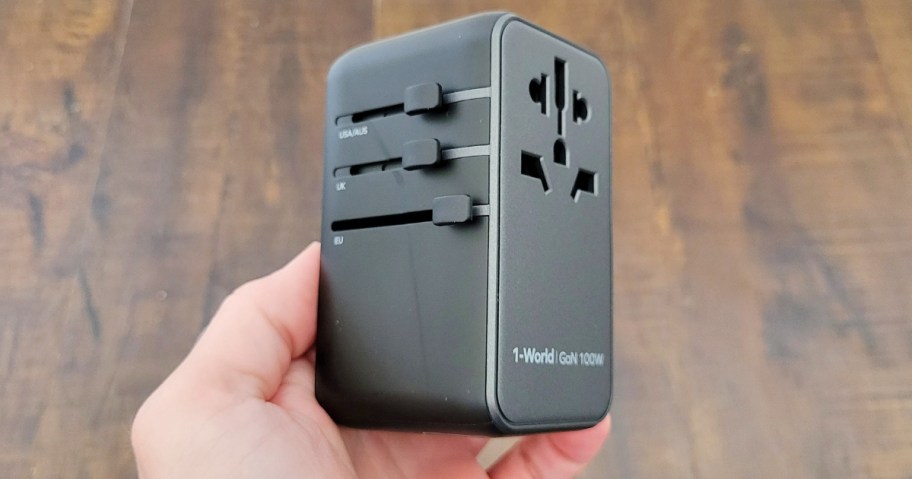 person's hand holding a 100W universal travel adapter