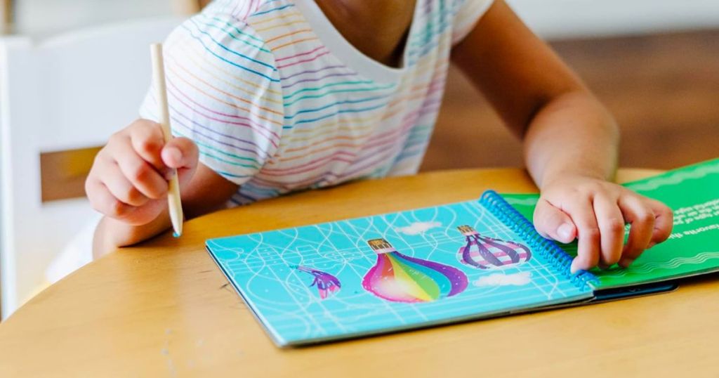 a little girls seated att a table with a Melissa & Doug On the Go Scratch Art Activity Books Set