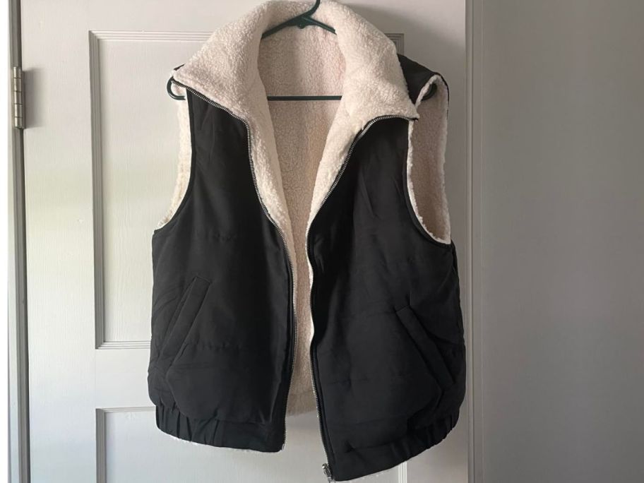 A black Prettygarden Sherpa Puffer Vest hanging on a hanger on a door