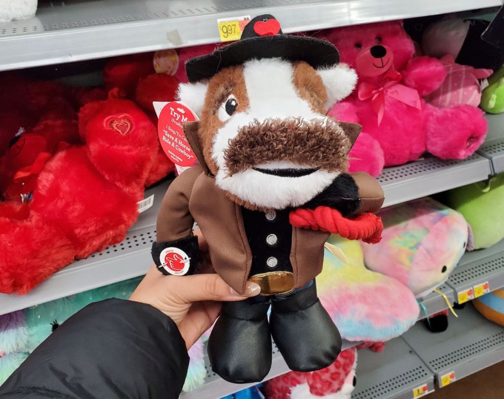 a womans hand displaying a brown and white animated horse plush wearing a cowboy hat and boots