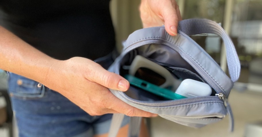 woman showing an open grey belt bag with the items inside to the camera