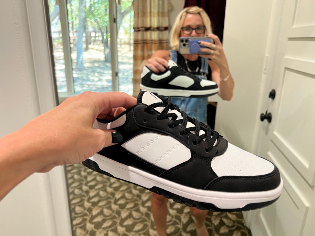 Woman holding up black and white sneaker and mirror