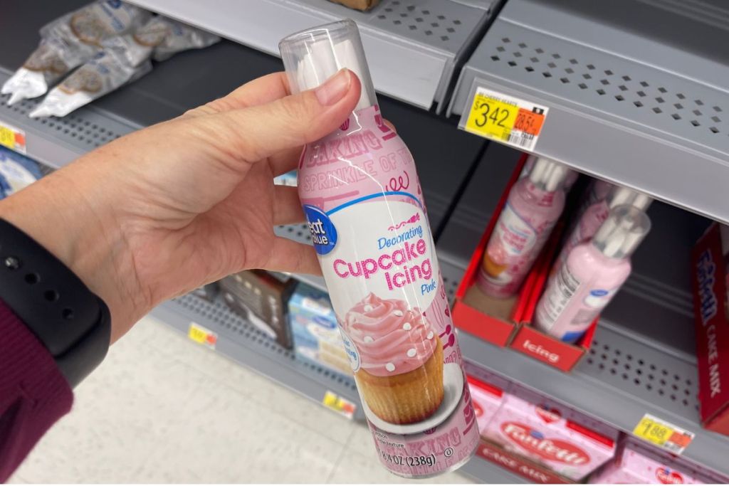 a womans hand holding a can of pink cupcake icing