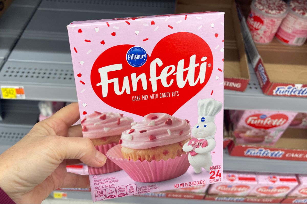 a woman's hand holding a box of funfetti cake mix in store