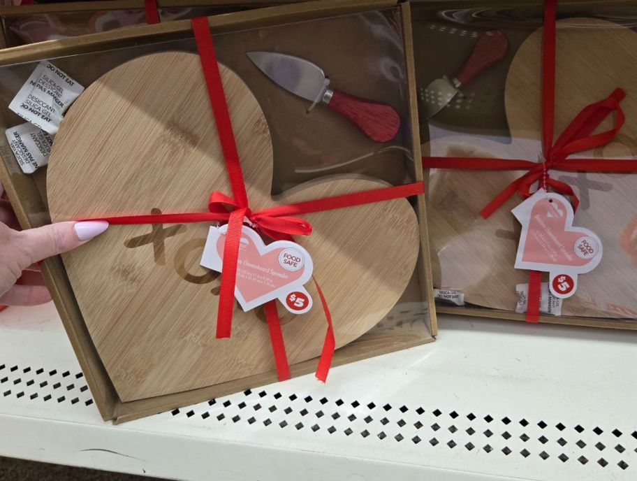 a womans hand grabbing a heart shaped charcuterie board set from a store shelf