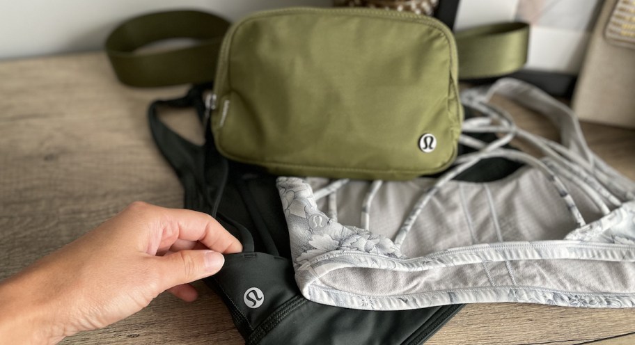 hand holding edge of black lululemon bra on dresser with other branded goods