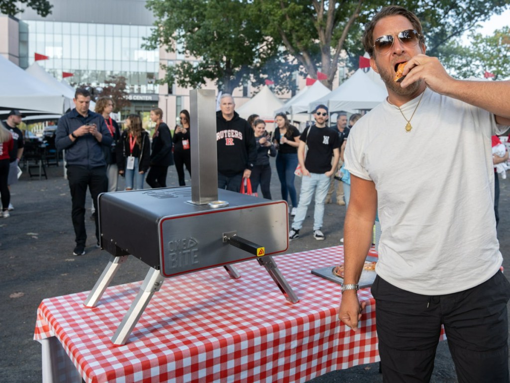 man taking a bite from pizza while standing next to one bite pizza open that is on top of a table