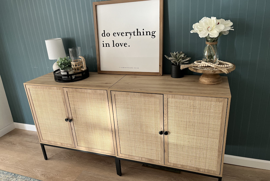 caned sideboard against dark green wall with various decor on top