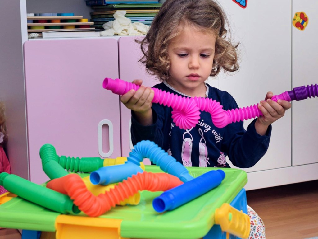 toddler holding up a twisted hot pink sensory tube