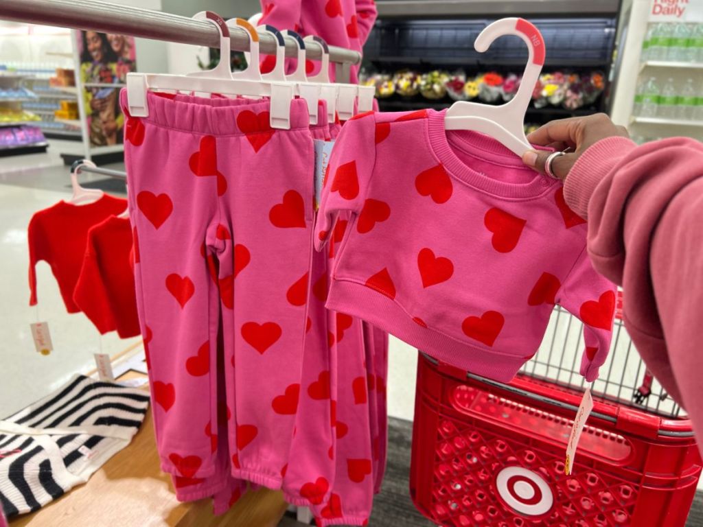 hand holding a pink toddler girls sweatshirt with red hearts next to a matching pair of pants