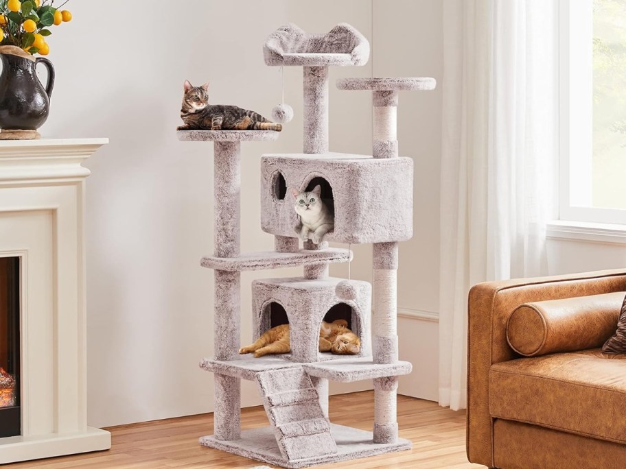 a light grey tall cat tower with cats in it and climbing on it in a living room