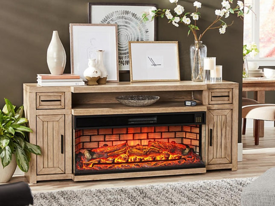 large light brown wood tv stand console with an electric fireplace in a living room with decor on it