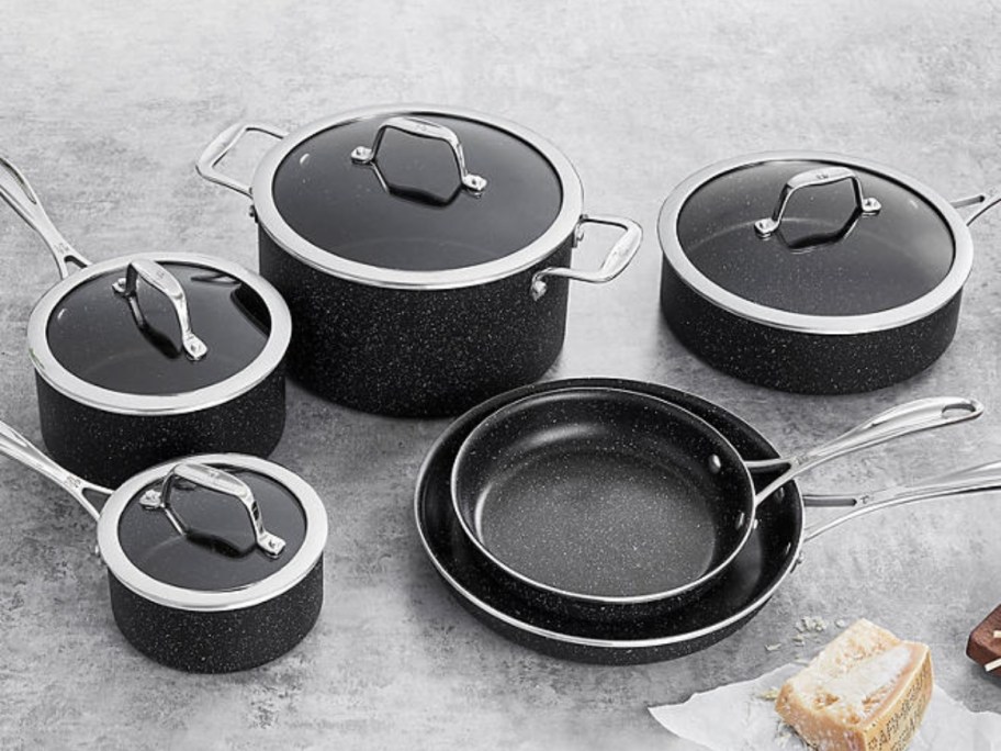 black cookware set with pots and pans and lids on a kitchen counter