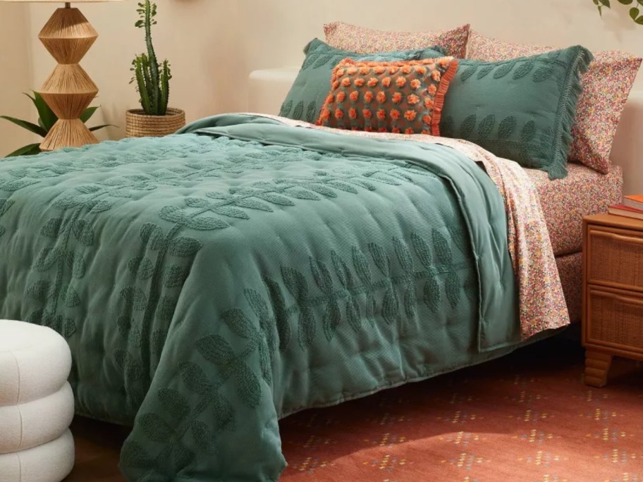 bed with teal green embroidered vine quilt, shams and decorative pillows