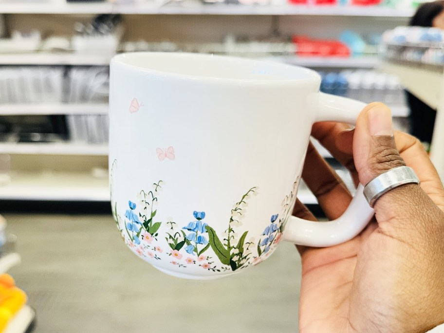 hand holding up a white coffee mugs with floral print around the bottom