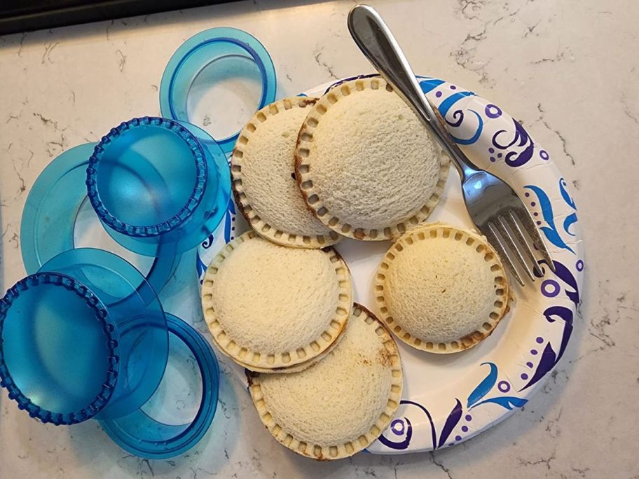 Sandwich Cutter in blue beside a few uncrustable sandwiches 