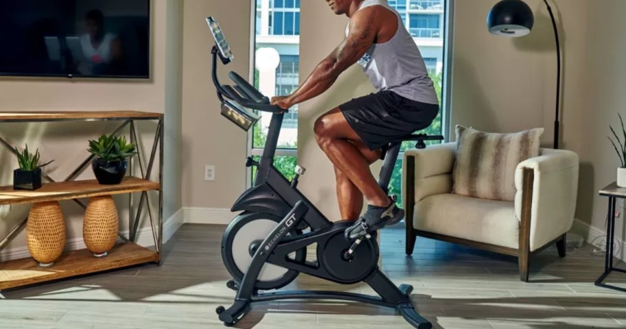 man riding a black indoor exercise bicycle in a living room