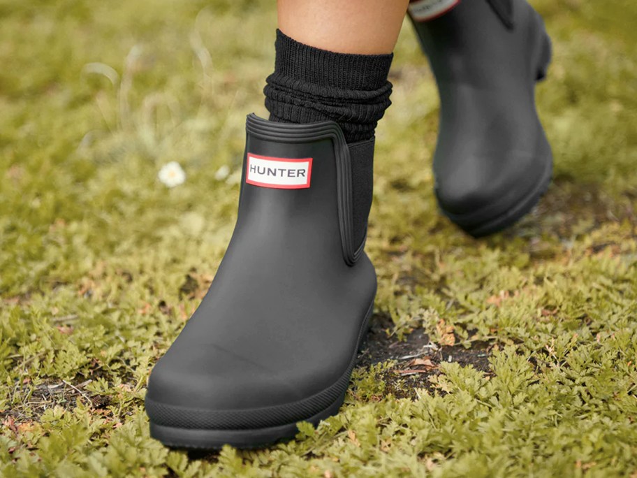 woman walking in grass wearing black Hunter Chelsea boots