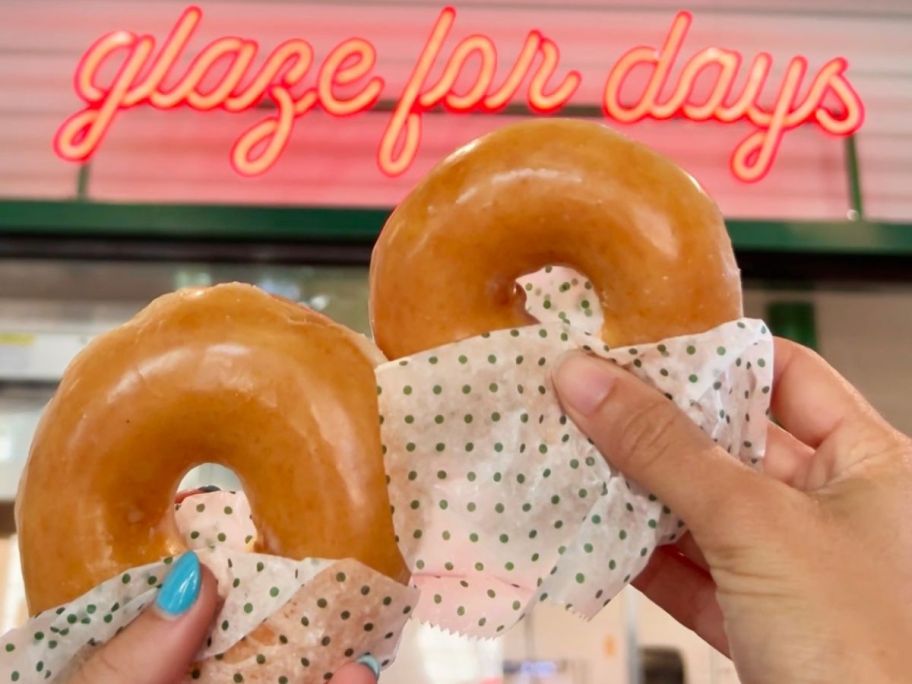 Hands holding up 2 Krispy Kreme Original Glazed Doughnuts