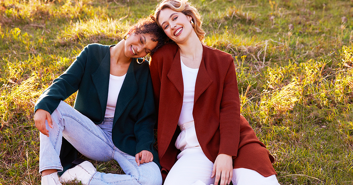 two women sitting in grass wearing dark green and orange coatigans