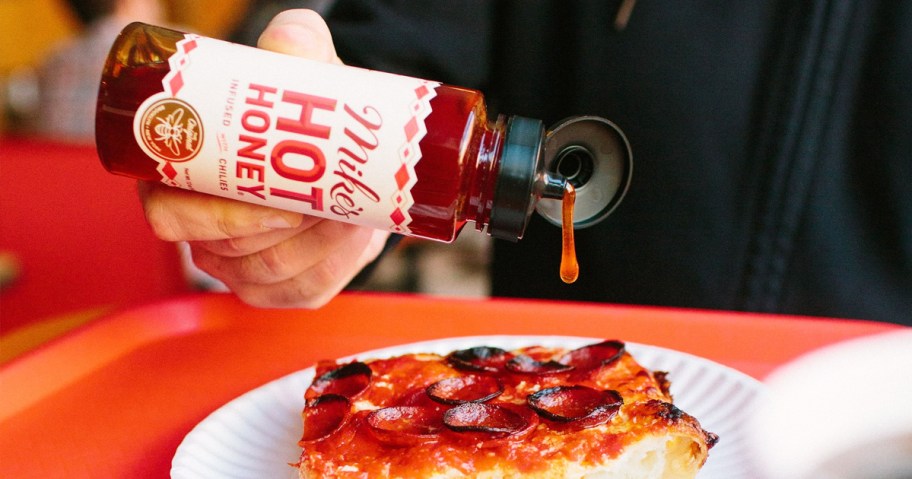 person pouring Mike's Hot Honey onto slice of pizza