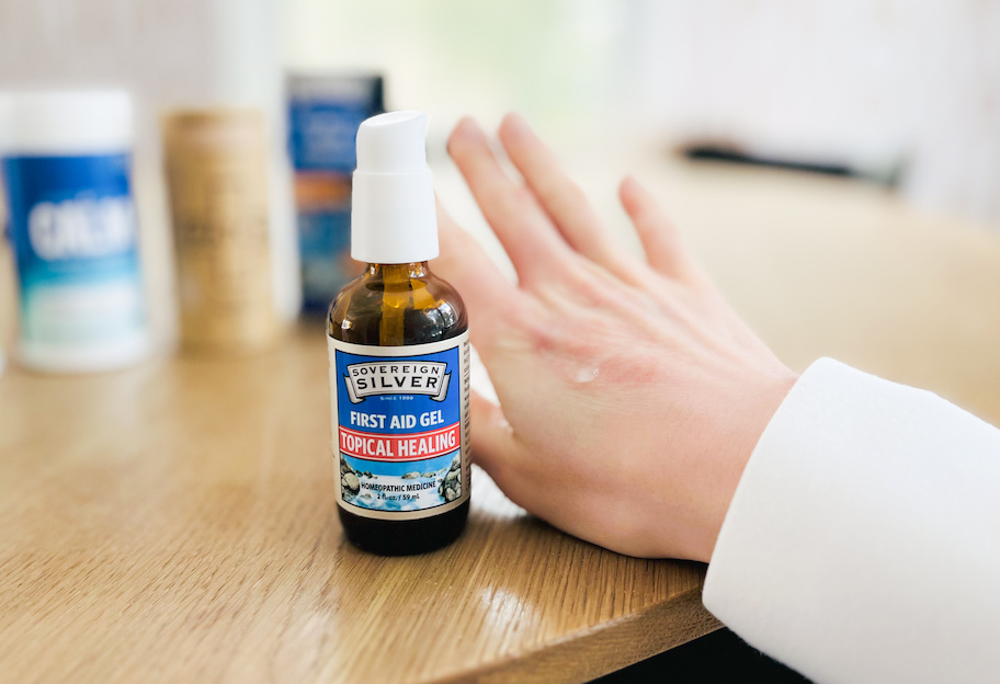 Hand with clear gel next to sovereign silver first aid gel bottle on the table