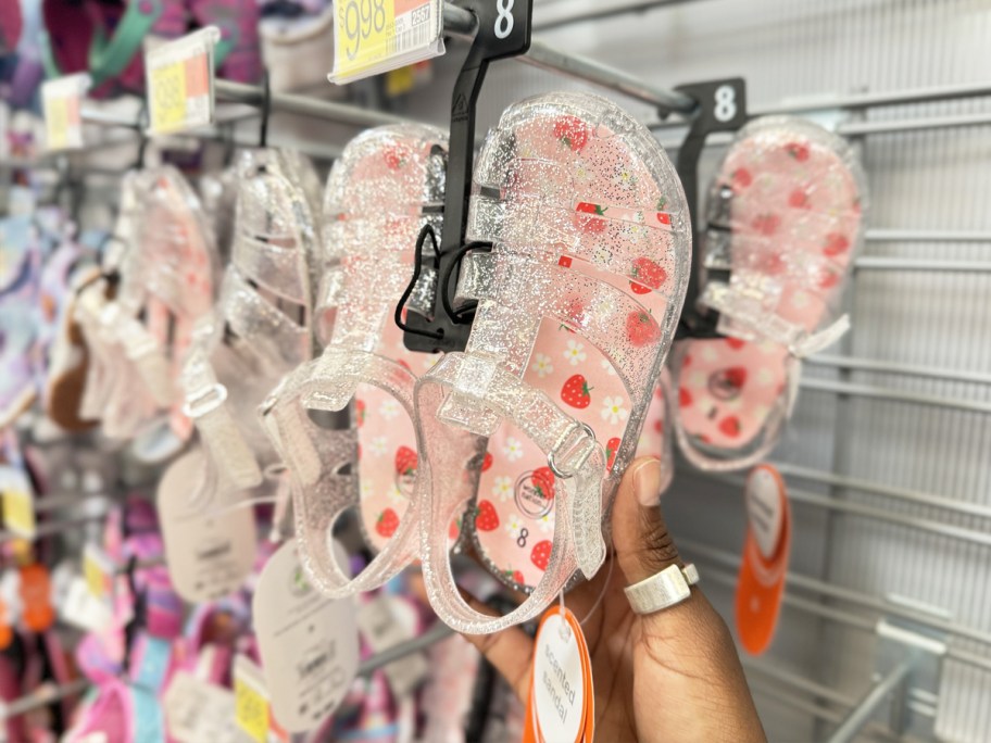 hand touching pair of glittery jelly sandals on store display rack