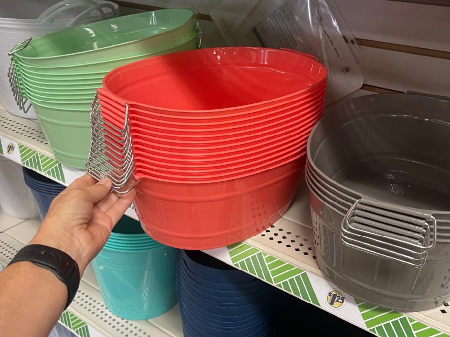 hand reaching for a reddish orange plastic bin with metal handles next to more in grey and green