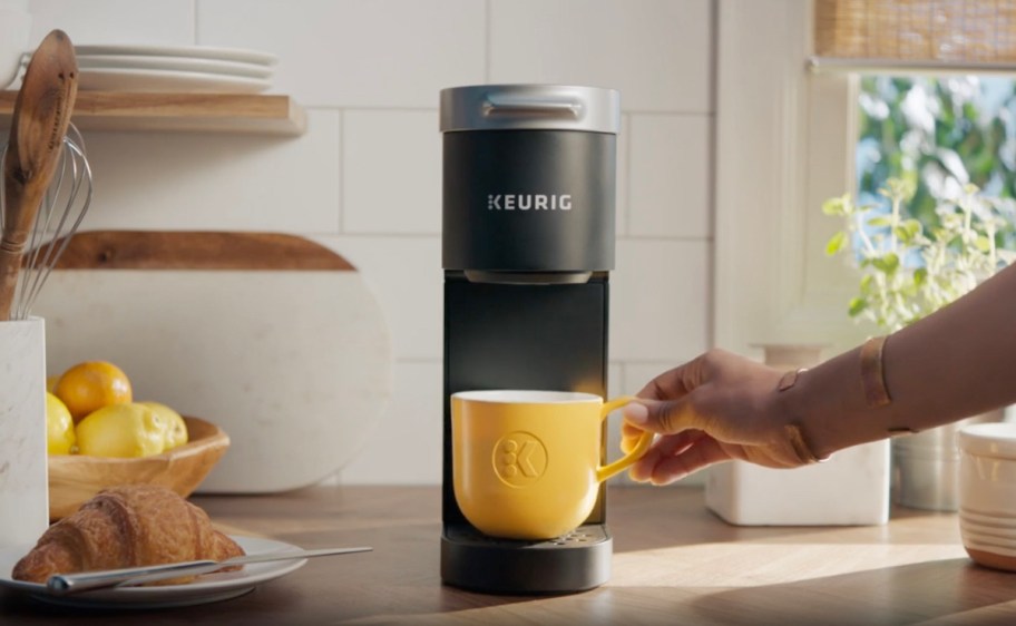 black keurig single serve coffee maker with hand putting yellow mug on it 