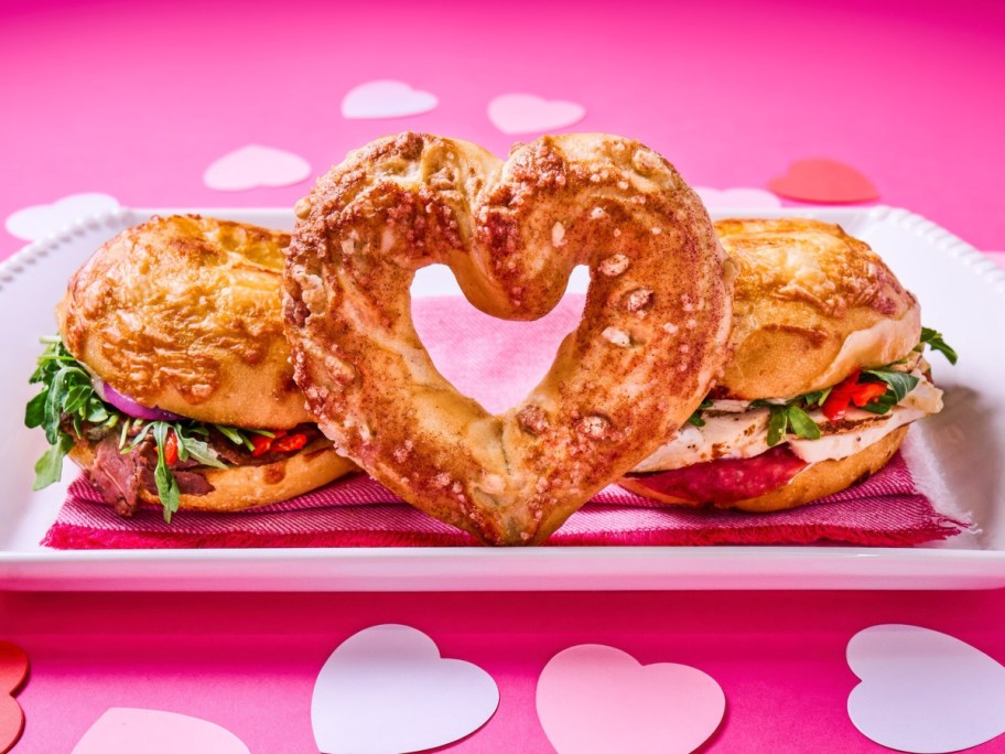 heart-shaped bagel on a plate next to 2 sandwiches