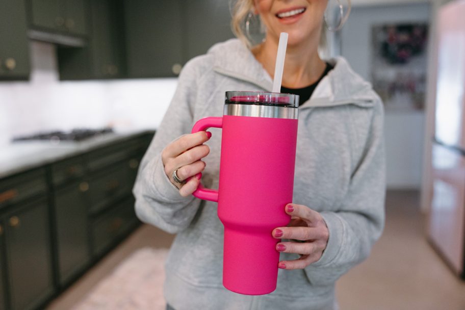 smiling woman standing in a kitchen holding a pink ozark trail tumbler with handle