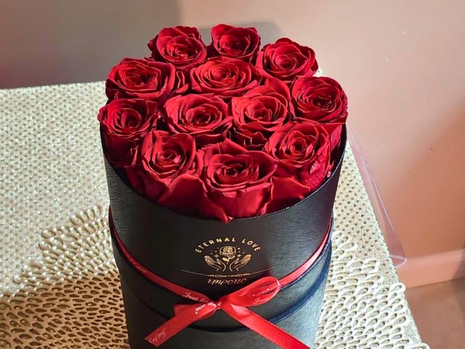 a black round box with gold lettering with several red roses in it sitting on a table