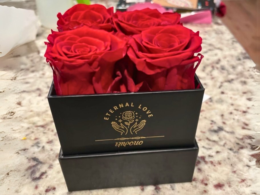 a black box with gold lettering on it, with red roses in it sitting on a countertop