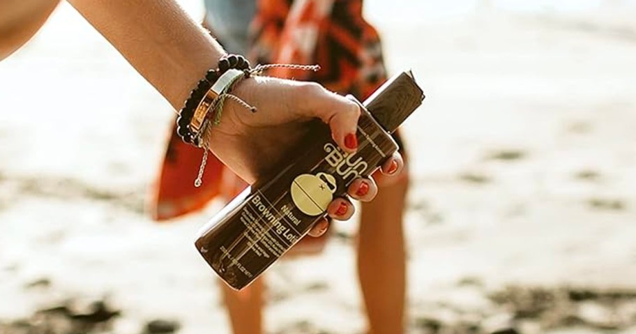 hand holding sun bum browning lotion bottle while walking on beach