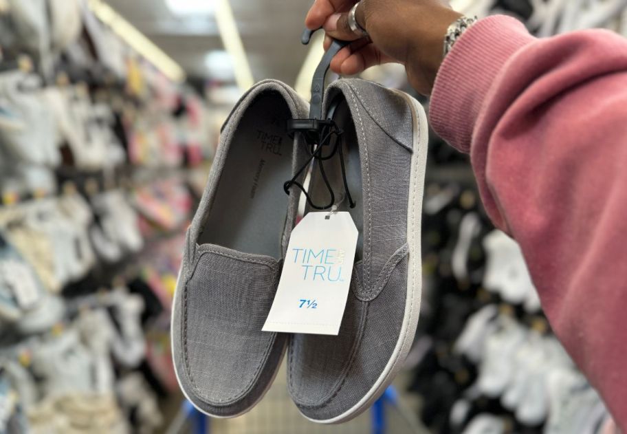 a womans hand holding a pair of gray time and tru canvas slip on shoes