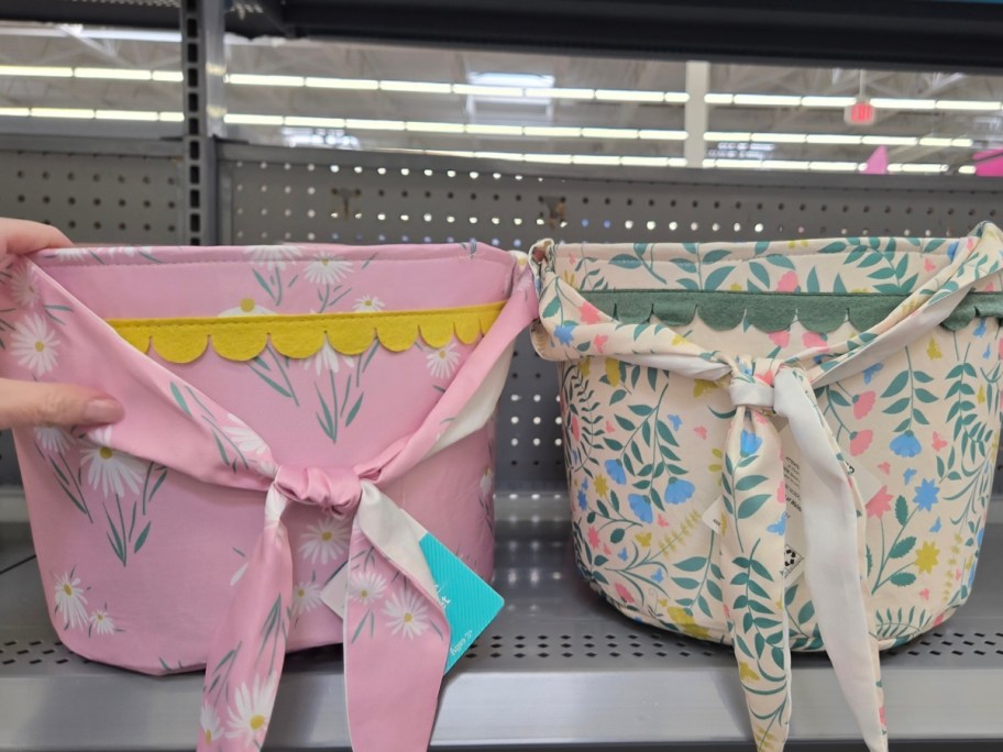 hand reaching for a pink floral fabric Easter basket on a store shelf, a white floral basket sits next to it