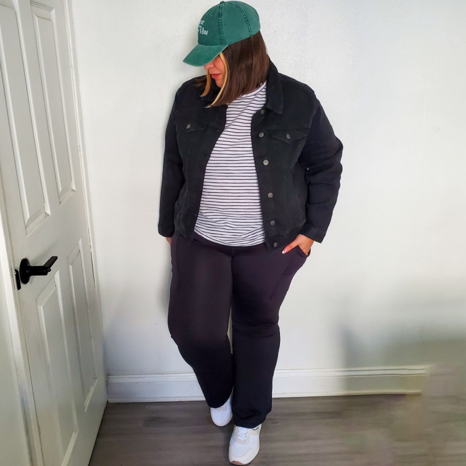 woman wearing black yoga pants, white striped tee, denim jacket, and green hat