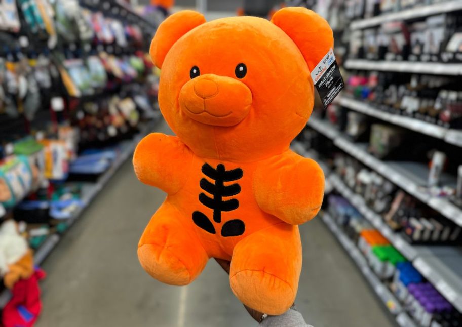 a womans hand holding an orange gummy bear plush