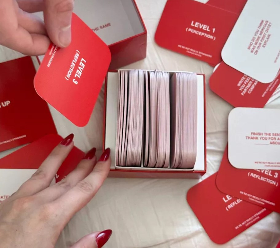 man and womans hands picking up red playing cards from box