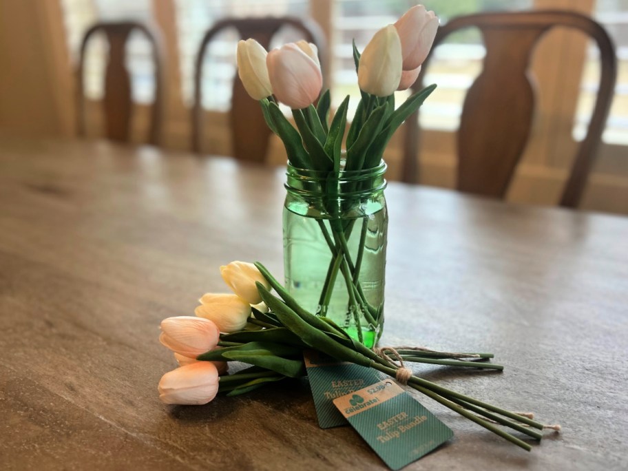 pink and white tulips inside green mason jar filled with water on wooden table top