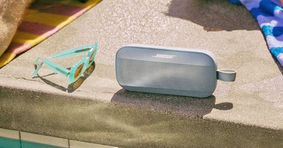 bose speaker on edge of pool near sunglasses