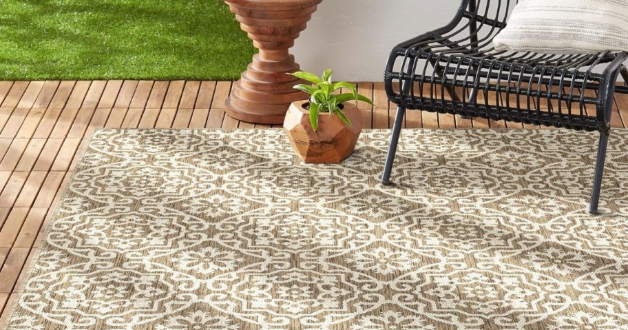 brown and beige rug on an outdoor patio with a black wrought iron chair, plan and side table