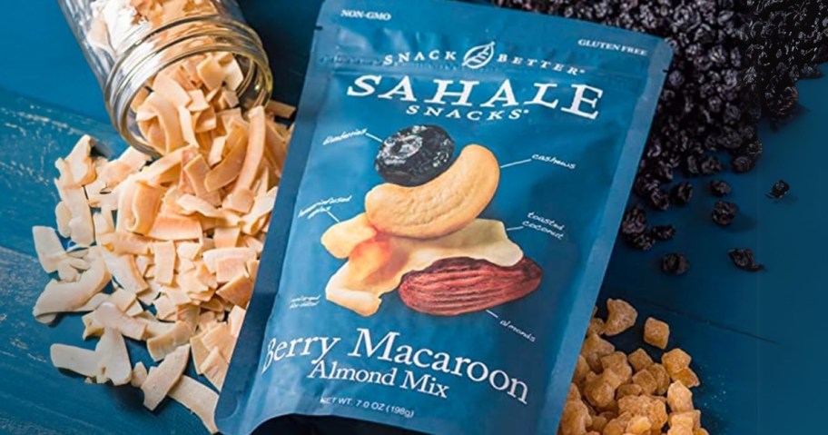 a blue bag of Sahale Snacks Berry Macaroon Almond Trail Mix on a counter with some of the mix, blueberries, and almond pieces behind it