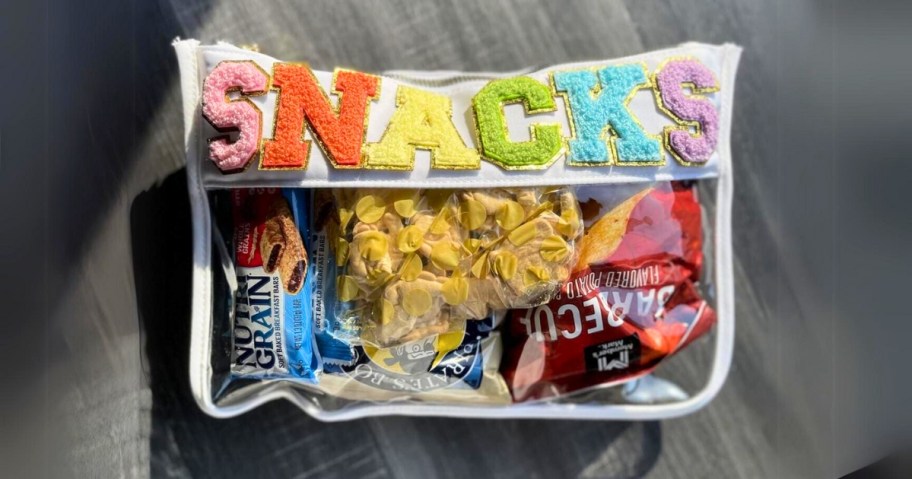 clear & white zipper bag with the word SNACKS in fuzzy block letters, bag is filled with various snacks