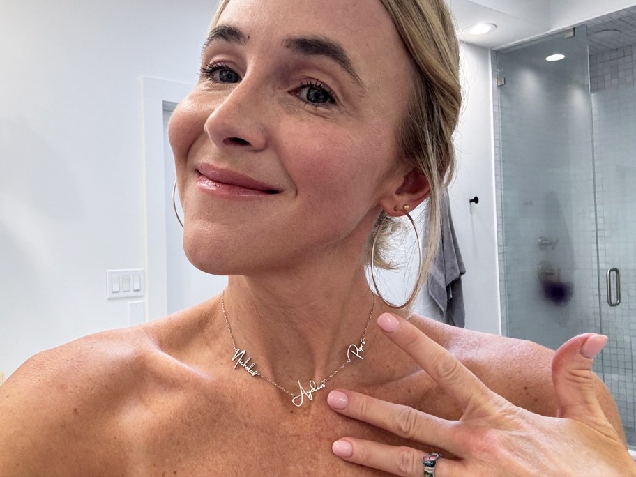 woman holding her hand up to the silver name necklace around her neck