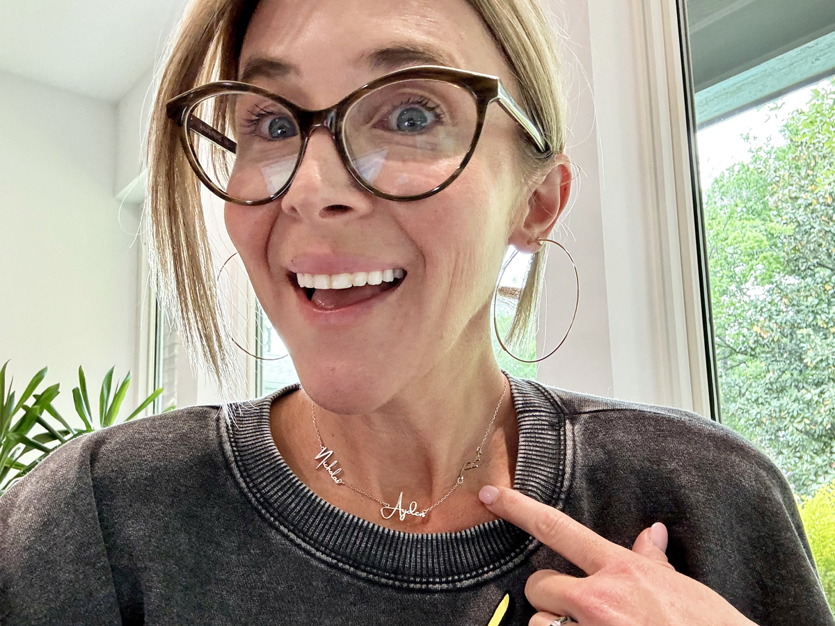 woman pointing to the silver name necklace around her neck