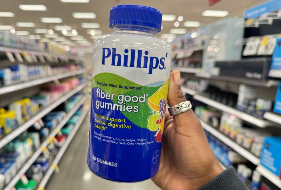 a womans hand holding a big bottle of phillips fiber gummies