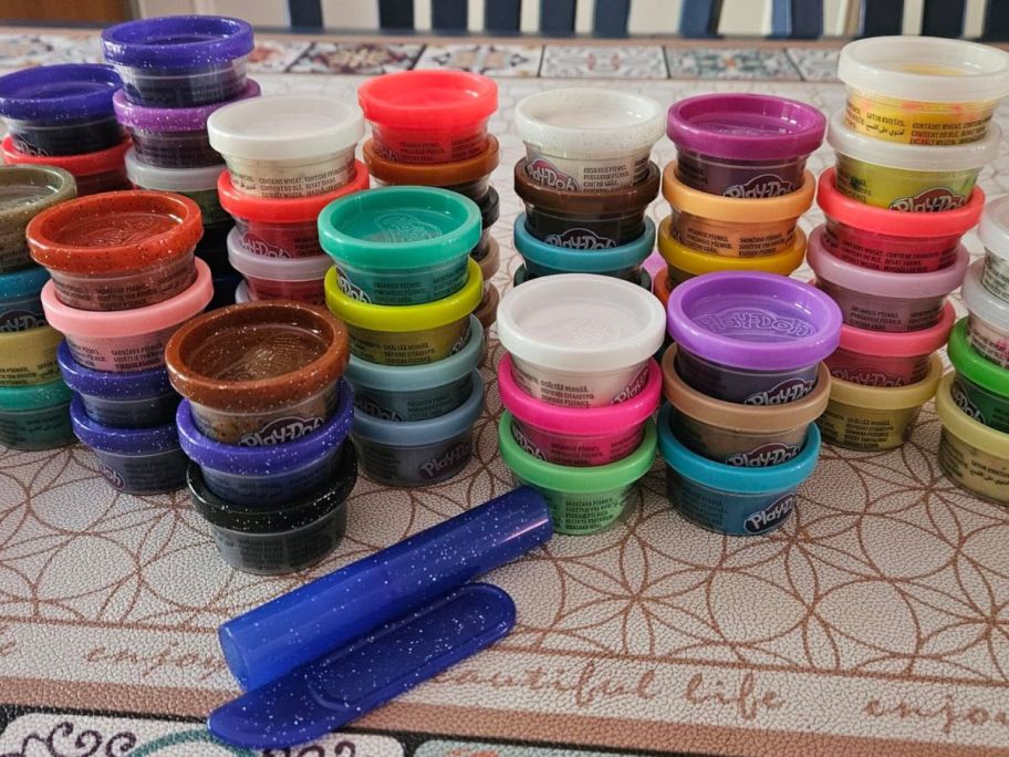 65 Play-Doh containers with a couple of cutting tools on a counter